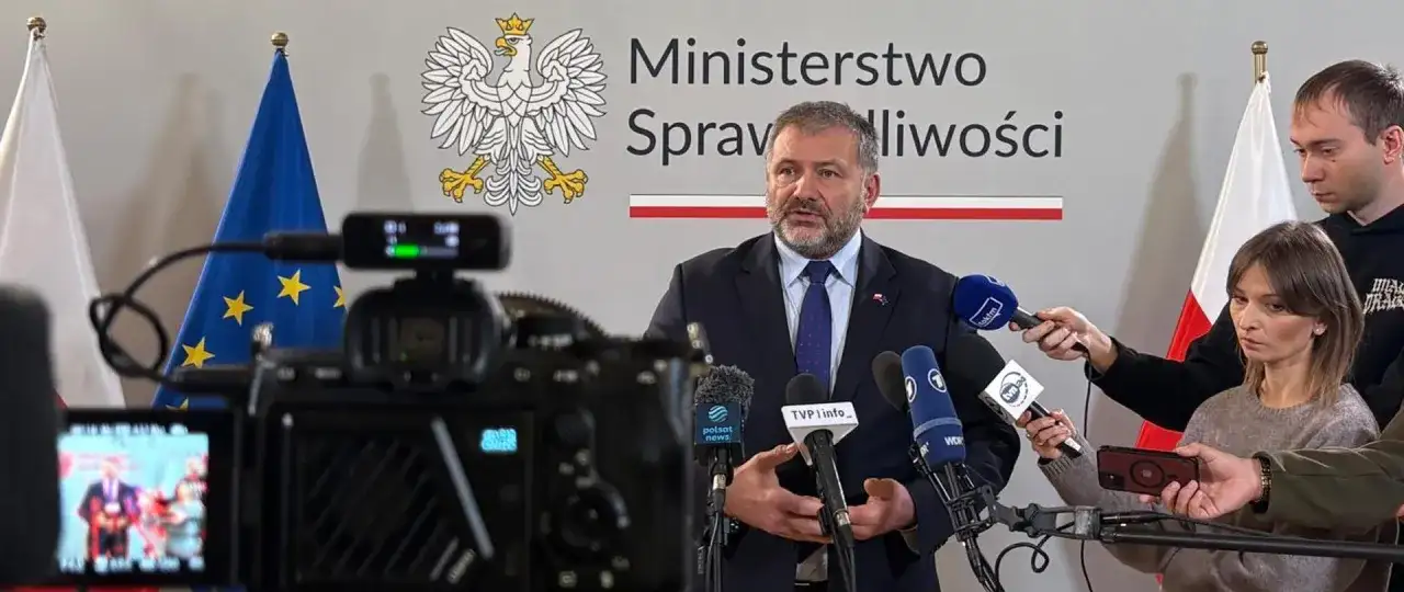 Minister sprawiedliwości przemawia do mediów, otoczony flagami Polski i UE. Dziennikarze zbierają materiał do reportażu o wyroku TSUE.