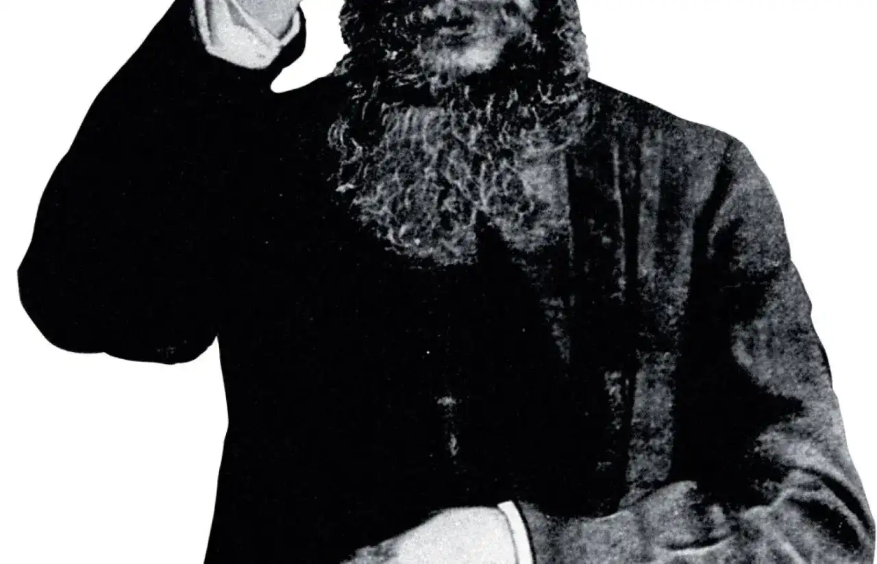 Grigorij Rasputin, z charakterystyczną brodą, wznosi rękę w geście błogosławieństwa lub pozdrowienia.