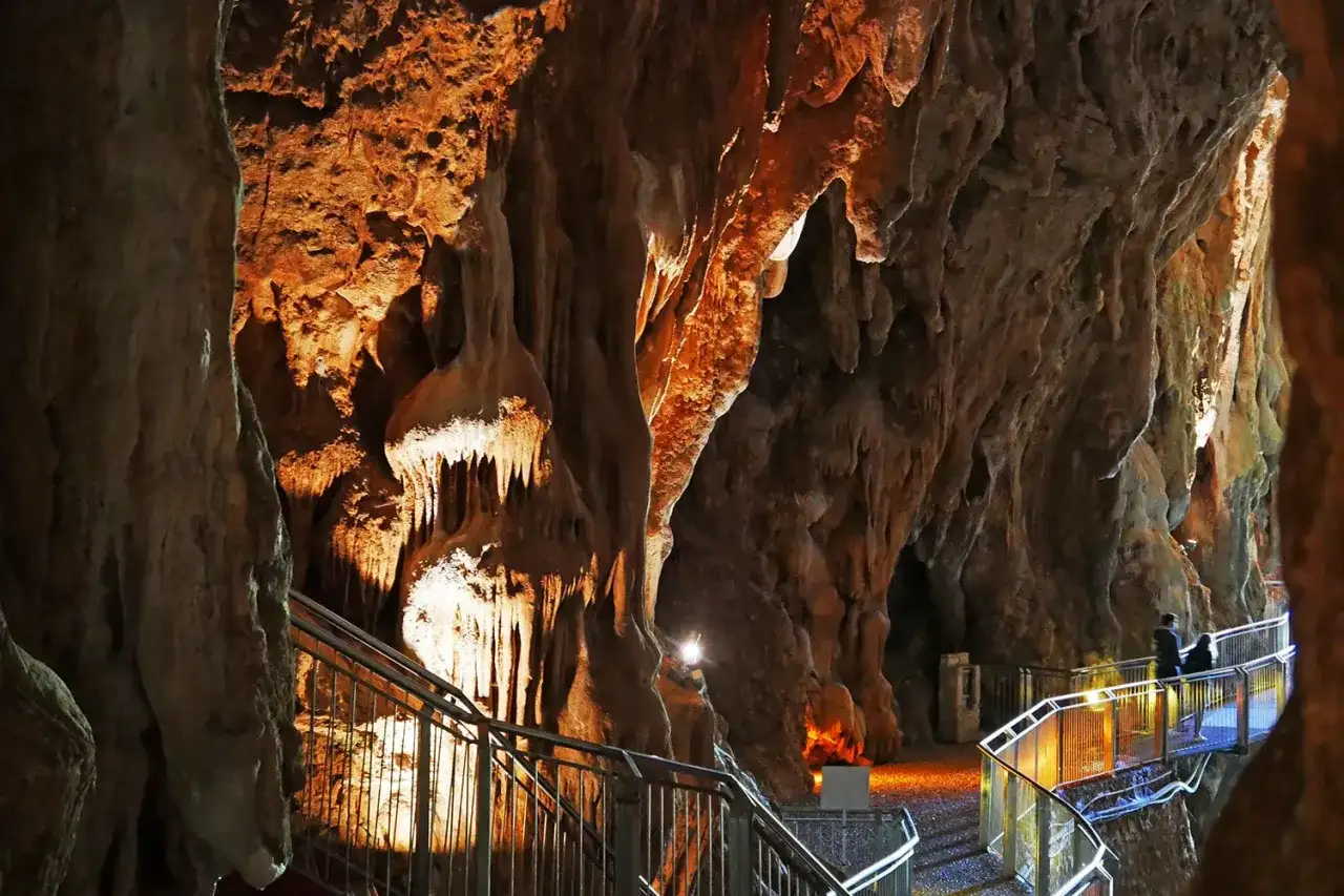 Sentiero illuminato tra le stalattiti delle grotte di Pastena, con persone che passeggiano.