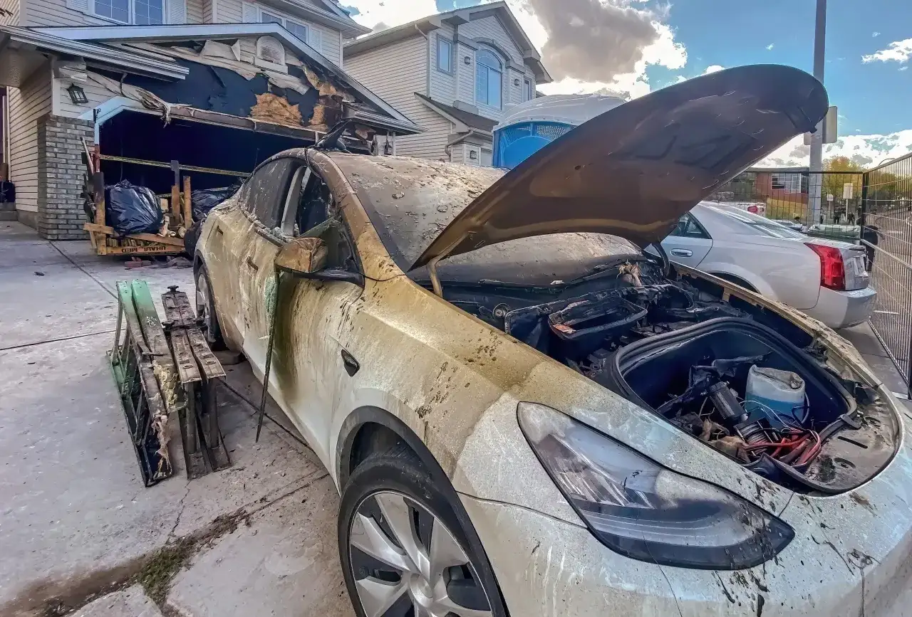 Spalony samochód elektryczny przed zniszczonym garażem. Może to być przyczyna, dlaczego w 2026 r. wzrosła liczba pożarów w warsztatach przez błędy w ładowaniu baterii.