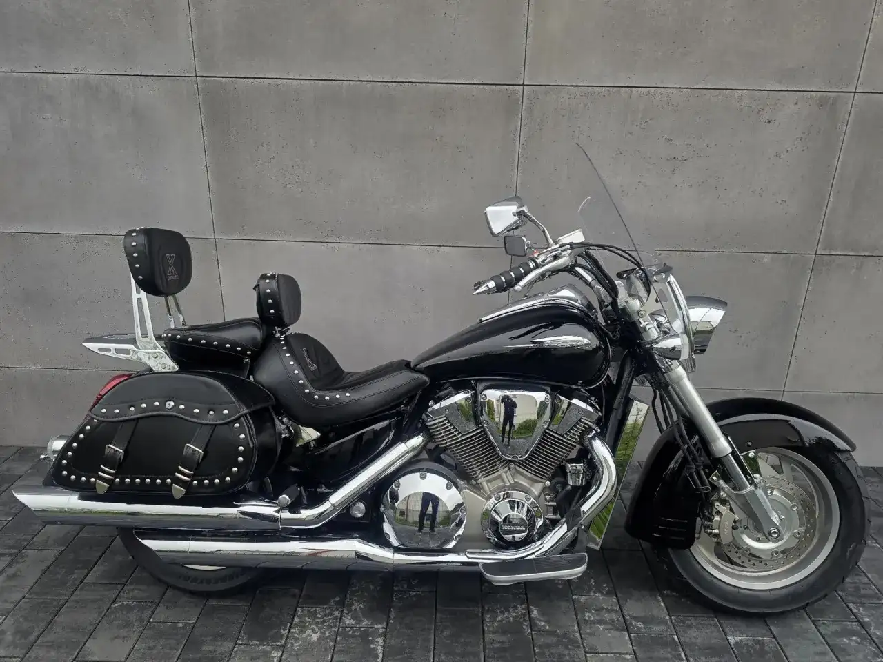 Czarny motocykl Honda VTX 1800 Neo z sakwami i oparciem dla pasażera, lśniący chromem na tle szarej ściany.
