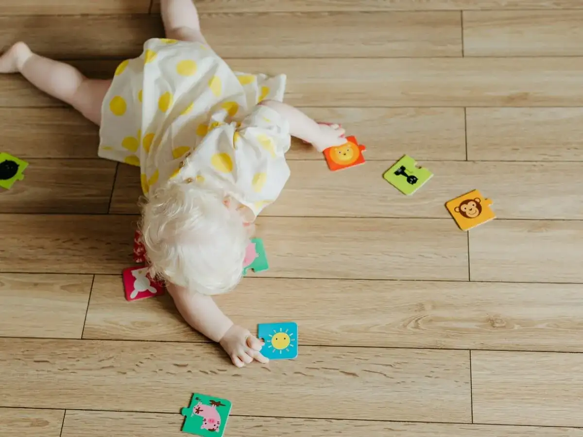 Dziecko z jasnymi włosami leży na podłodze, otoczone kolorowymi puzzlami ze zwierzątkami. Zastanawiasz się, dlaczego dziecko buczy? Może nie może dopasować puzzla z uśmiechniętym słoneczkiem.