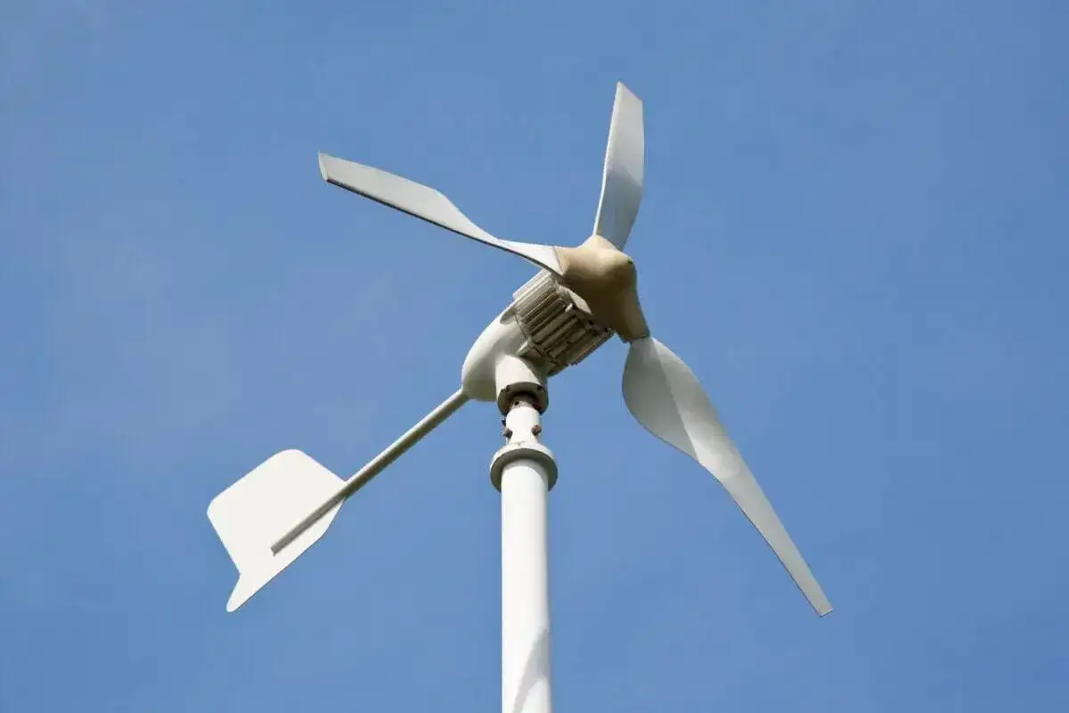 Moja elektrownia wiatrowa, biała turbina z trzema łopatami, obraca się na tle błękitnego nieba, czerpiąc energię z wiatru.