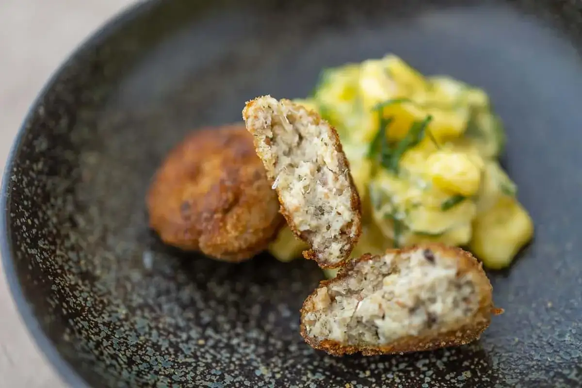 Zwei goldbraune Fischbuletten, eine aufgeschnitten, daneben Kartoffelsalat. Ein leckeres Fischbuletten Rezept.