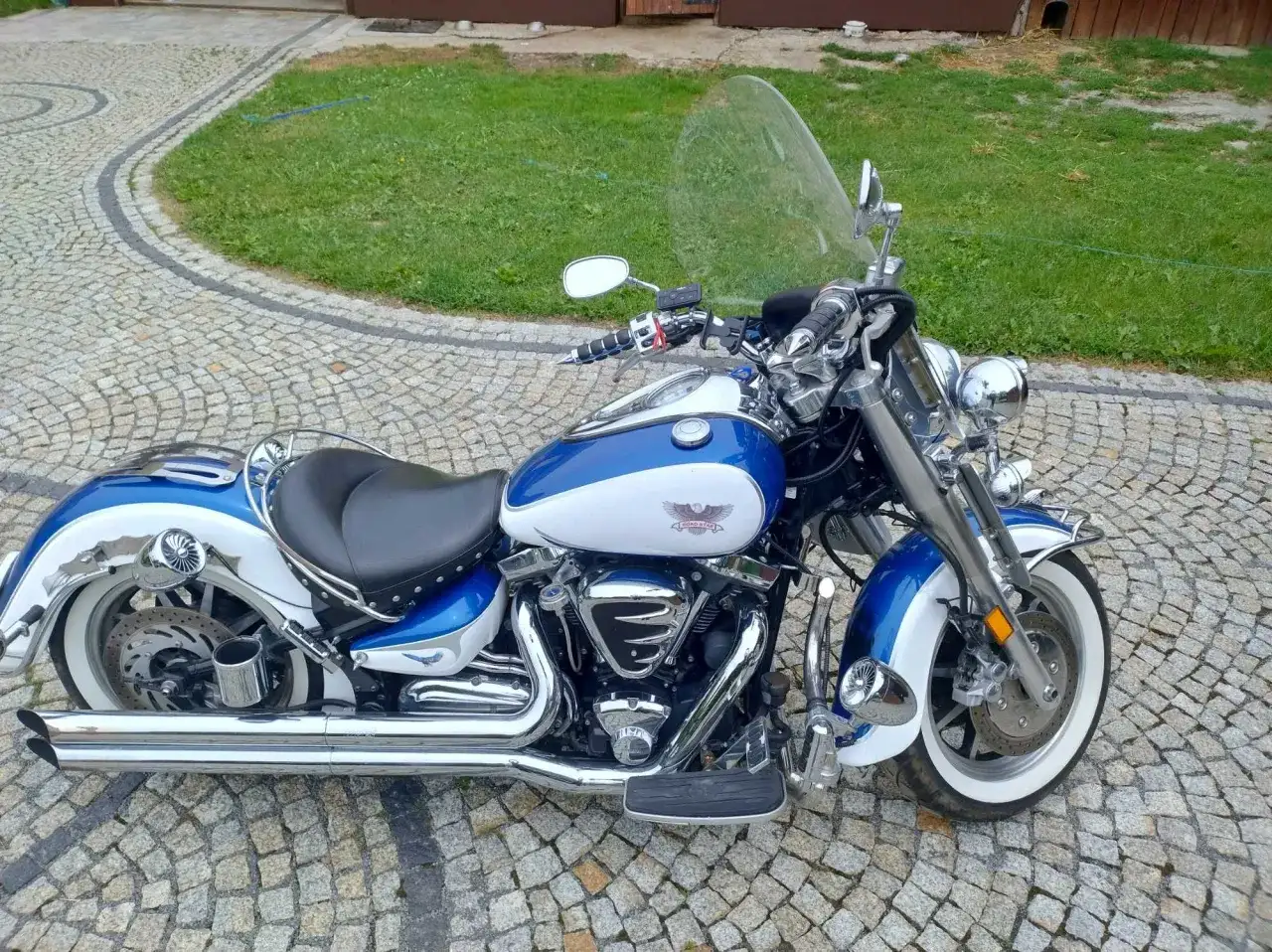 Błękitno-biały Yamaha Road Star 1700 lśni chromem na brukowanym podjeździe, gotowy na przygodę.