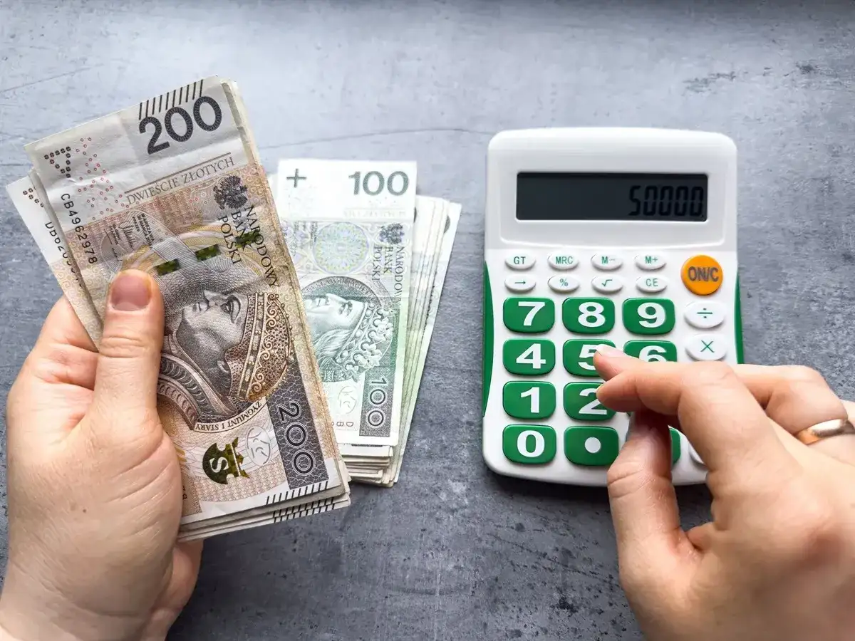 Ręka trzyma banknoty 200 zł i 100 zł, obok kalkulator z wyświetloną kwotą 50000. Czy to już minimalna krajowa?