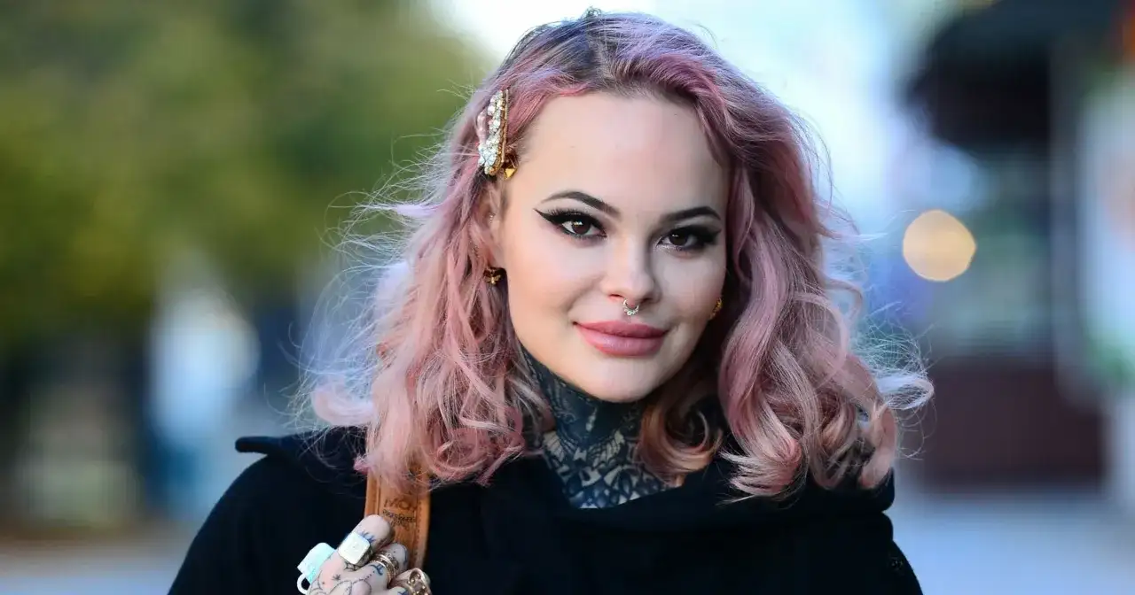 Monika Miller z różowymi włosami i tatuażami na szyi, mimo choroby, uśmiecha się do obiektywu.