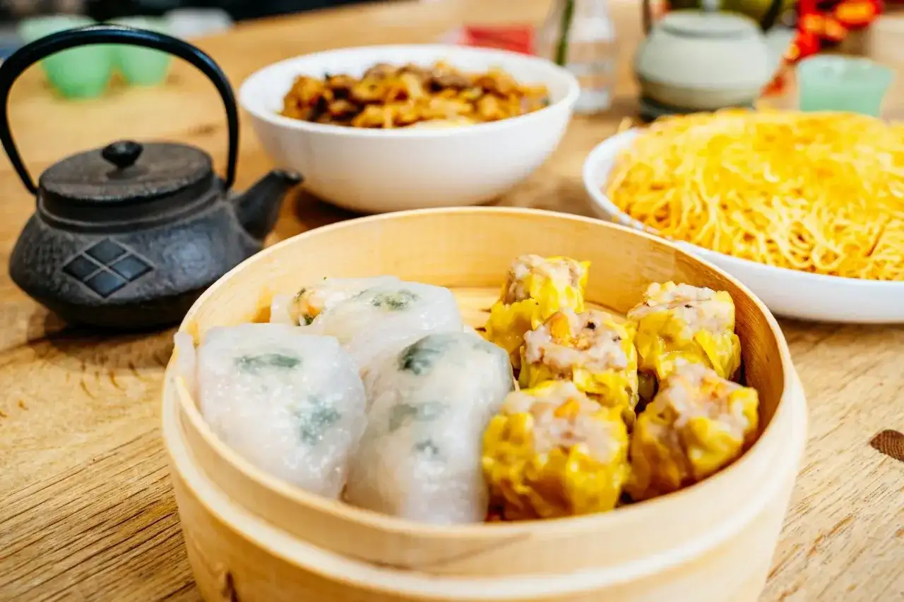 Pyszne dim sum w bambusowym parowniku, obok miseczki z makaronem i daniem mięsnym.