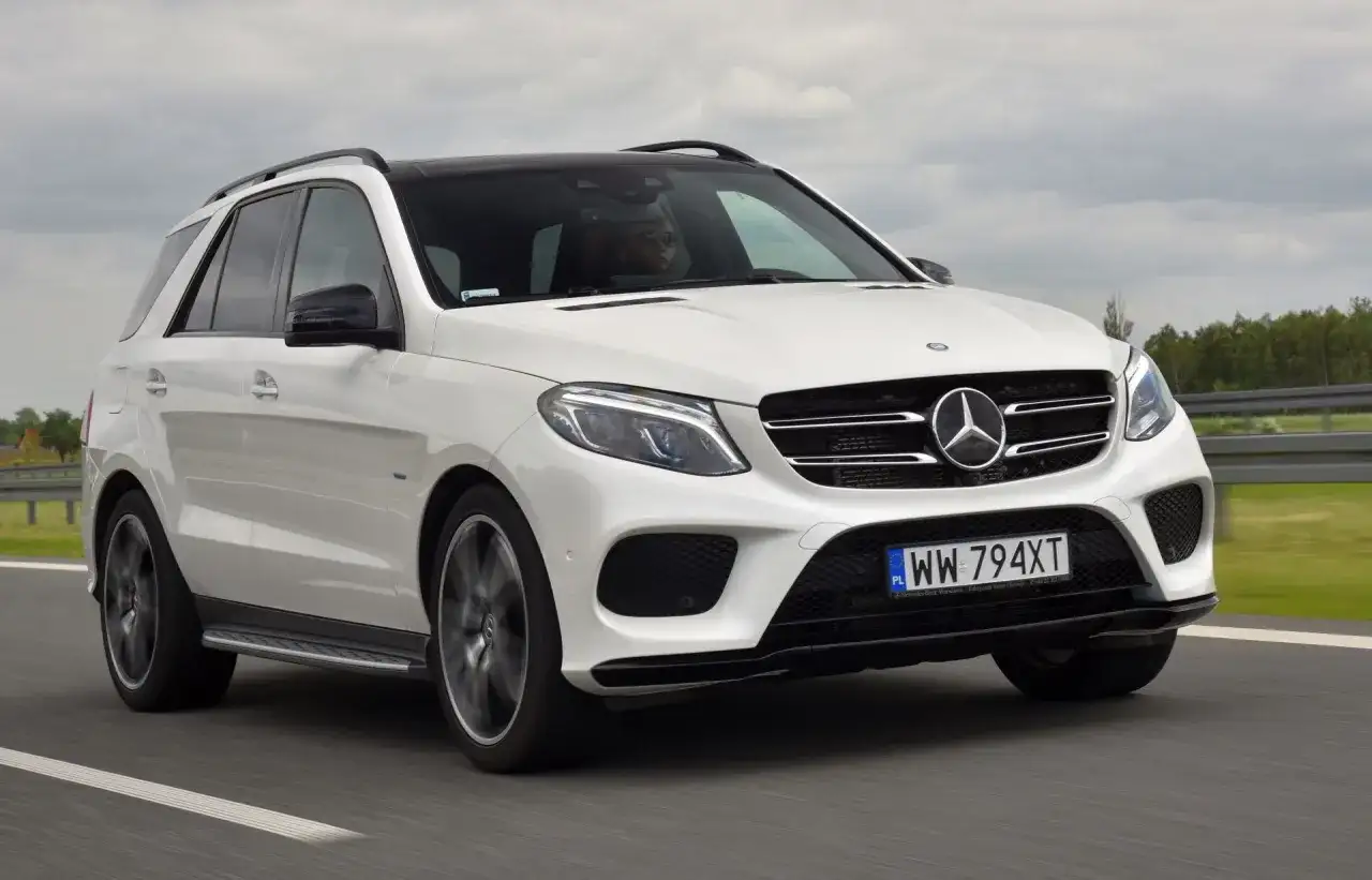 Biały Mercedes GLE 400d z czarnym dachem pędzi po drodze. Kierowca w okularach prowadzi auto.