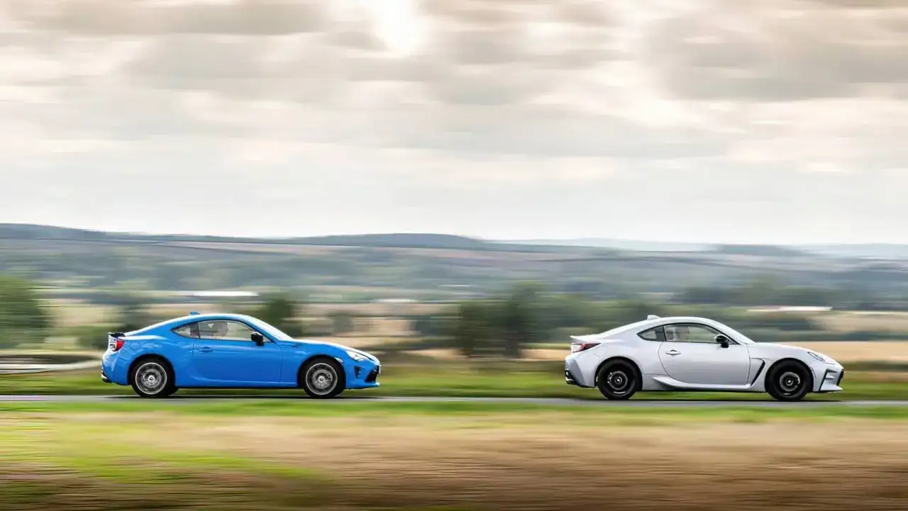 Dwa sportowe samochody, niebieska i srebrna Toyota 86, pędzą po wiejskiej drodze, tworząc dynamiczny obraz.