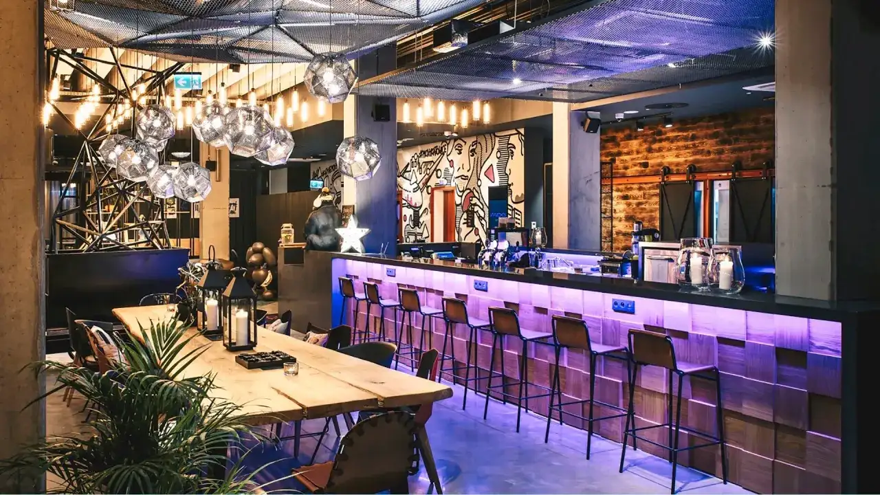 Nowoczesny bar w Moxy Hotels Pyrzowice z neonowym oświetleniem, drewnianym blatem i artystycznymi muralami.