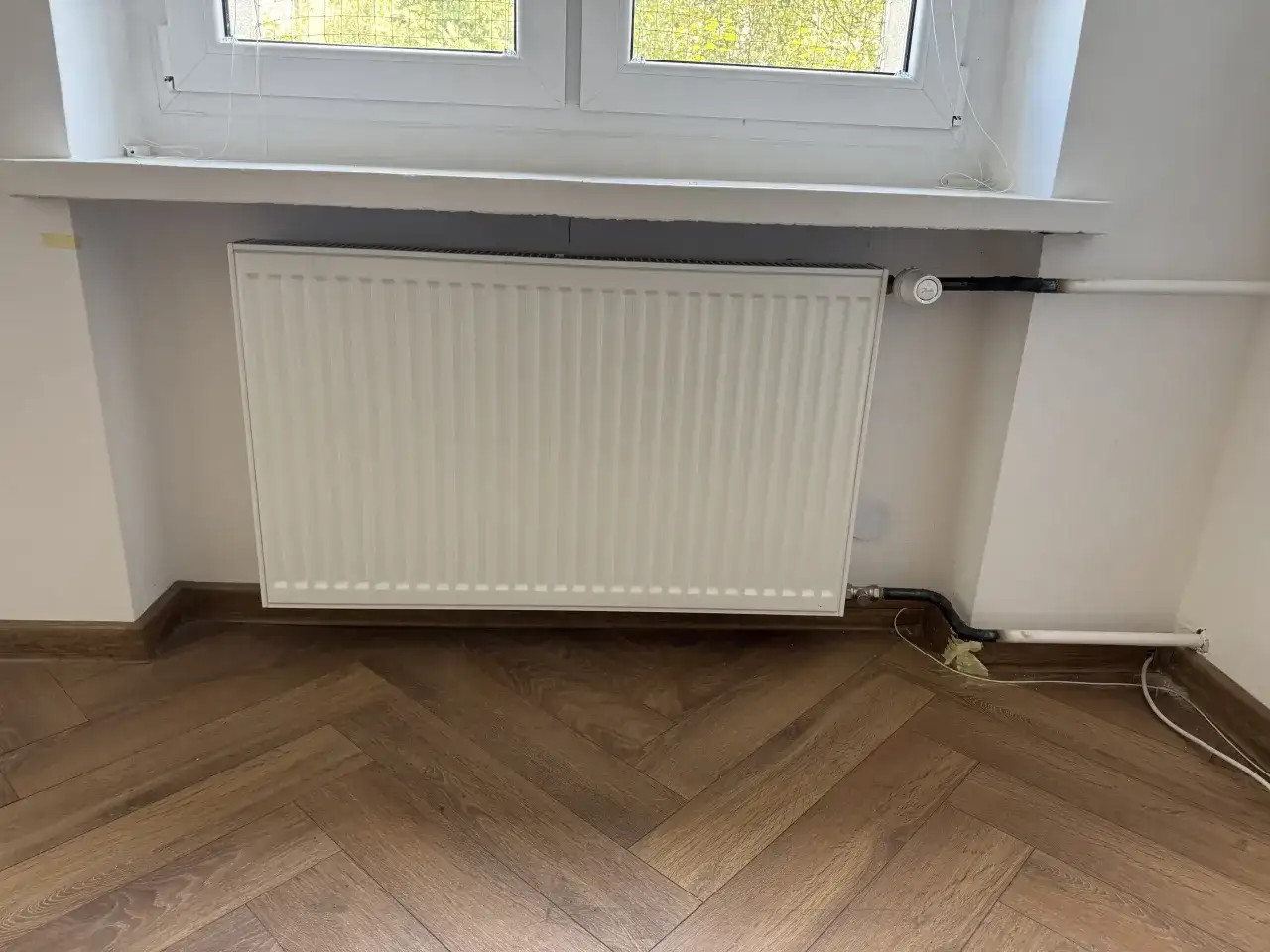 Biały grzejnik pod oknem, nowe podłączenie. Zastanawiasz się, ile kosztuje wymiana kaloryfera?