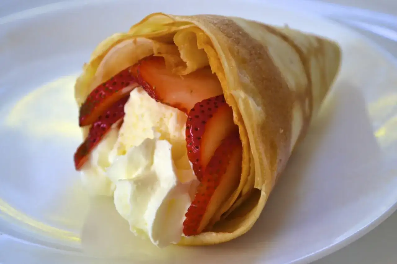 Délicieuse crêpe japonaise moelleuse garnie de fraises fraîches et de crème fouettée, servie sur une assiette blanche.