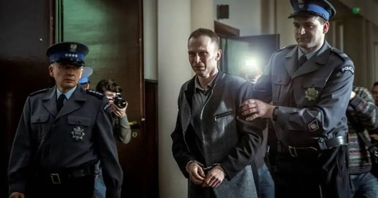 Scena z filmu o Tomaszu Komendzie: policjanci eskortują go w kajdankach, a za nimi stoi fotograf z aparatem.