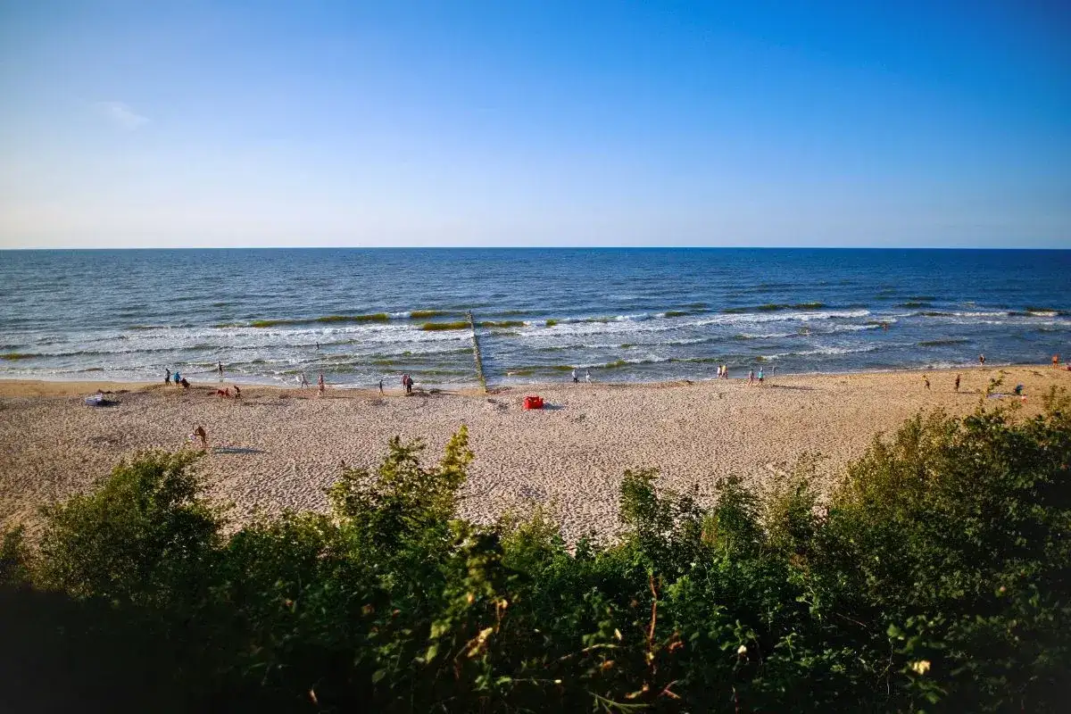 Słoneczna plaża, morze i ludzie spacerujący brzegiem. Dziwnówek atrakcje to idealne miejsce na letni wypoczynek.