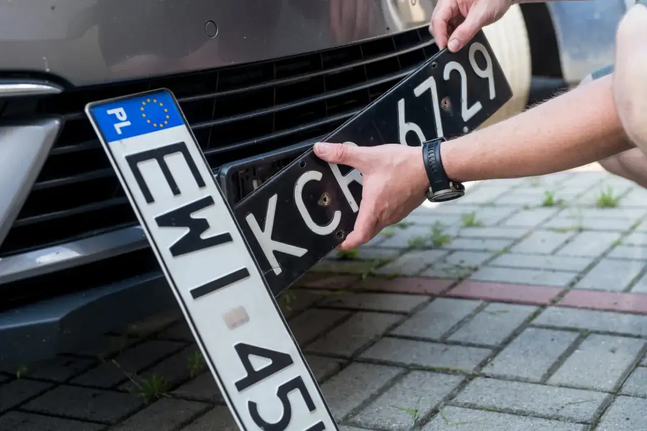 Ręce montują tablicę rejestracyjną do samochodu. Nowa elc rejestracja czeka na zamontowanie.