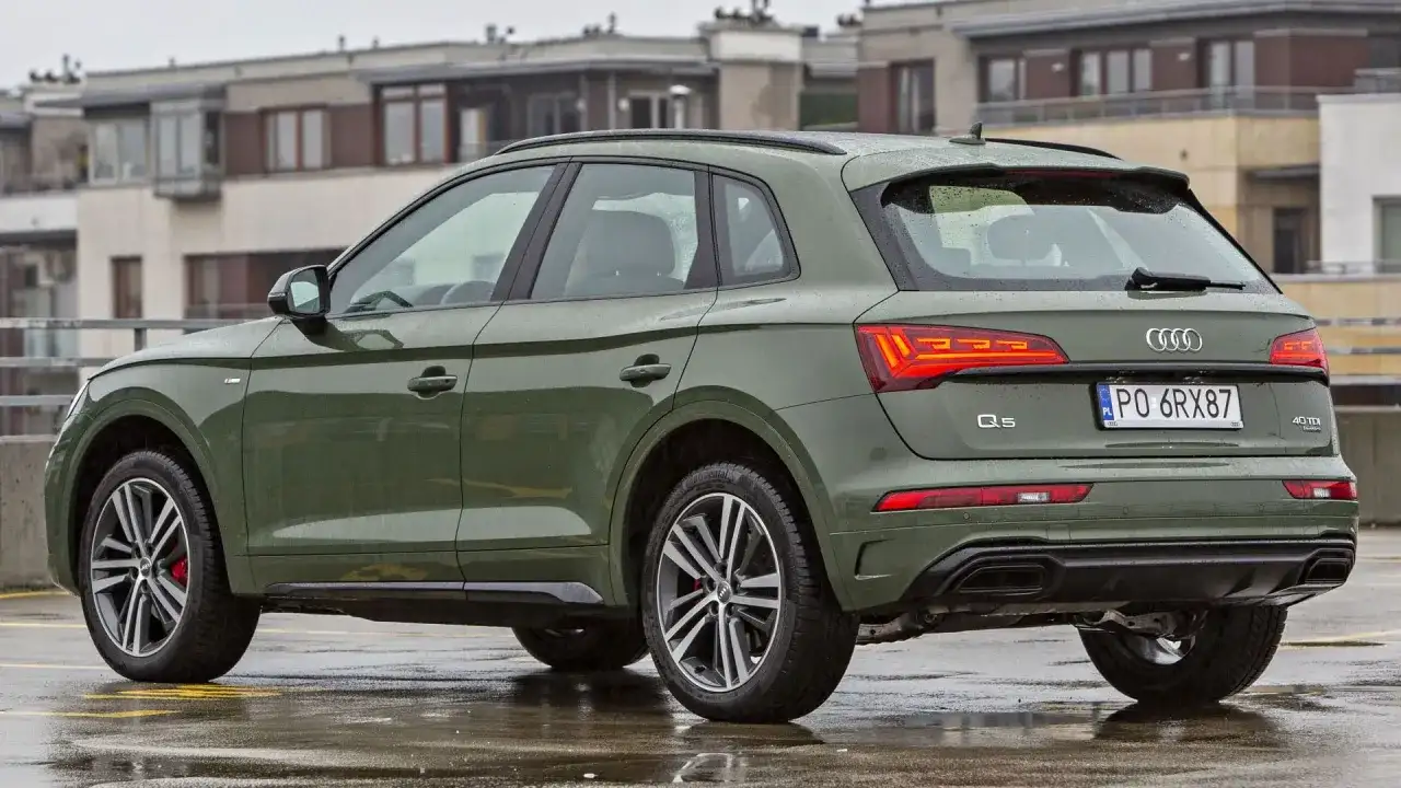 Zielony Audi Q5 Sportback na mokrym parkingu, z budynkami w tle.