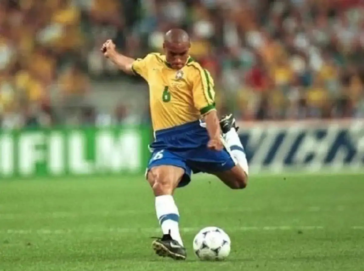 Roberto Carlos, z numerem 6 na koszulce, wykonuje potężne uderzenie piłki na boisku.