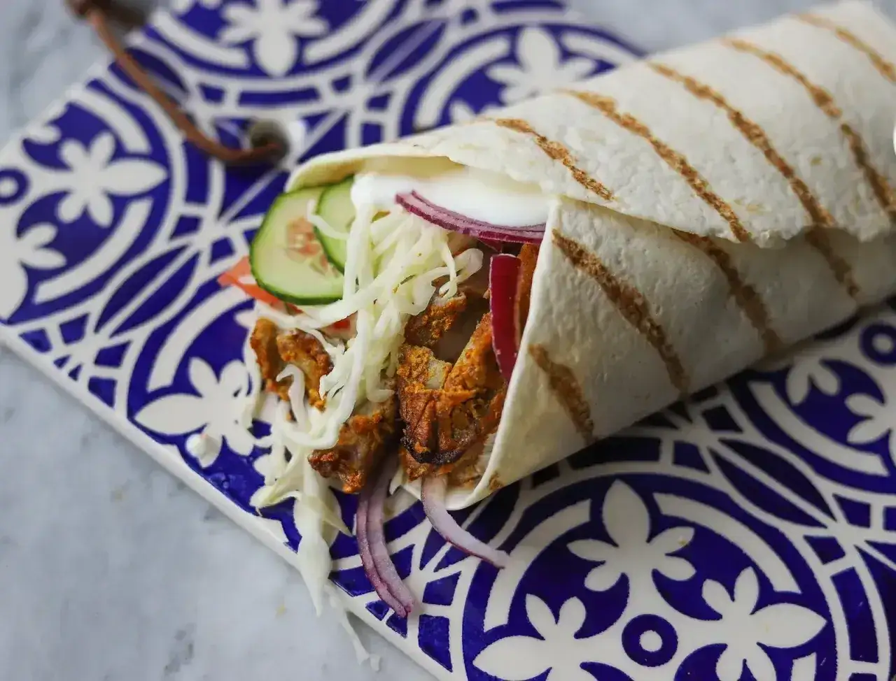 Pyszny kebab w picie z soczystym mięsem, chrupiącą surówką, pomidorem, ogórkiem i czerwoną cebulą, zawinięty w ciepły placek.