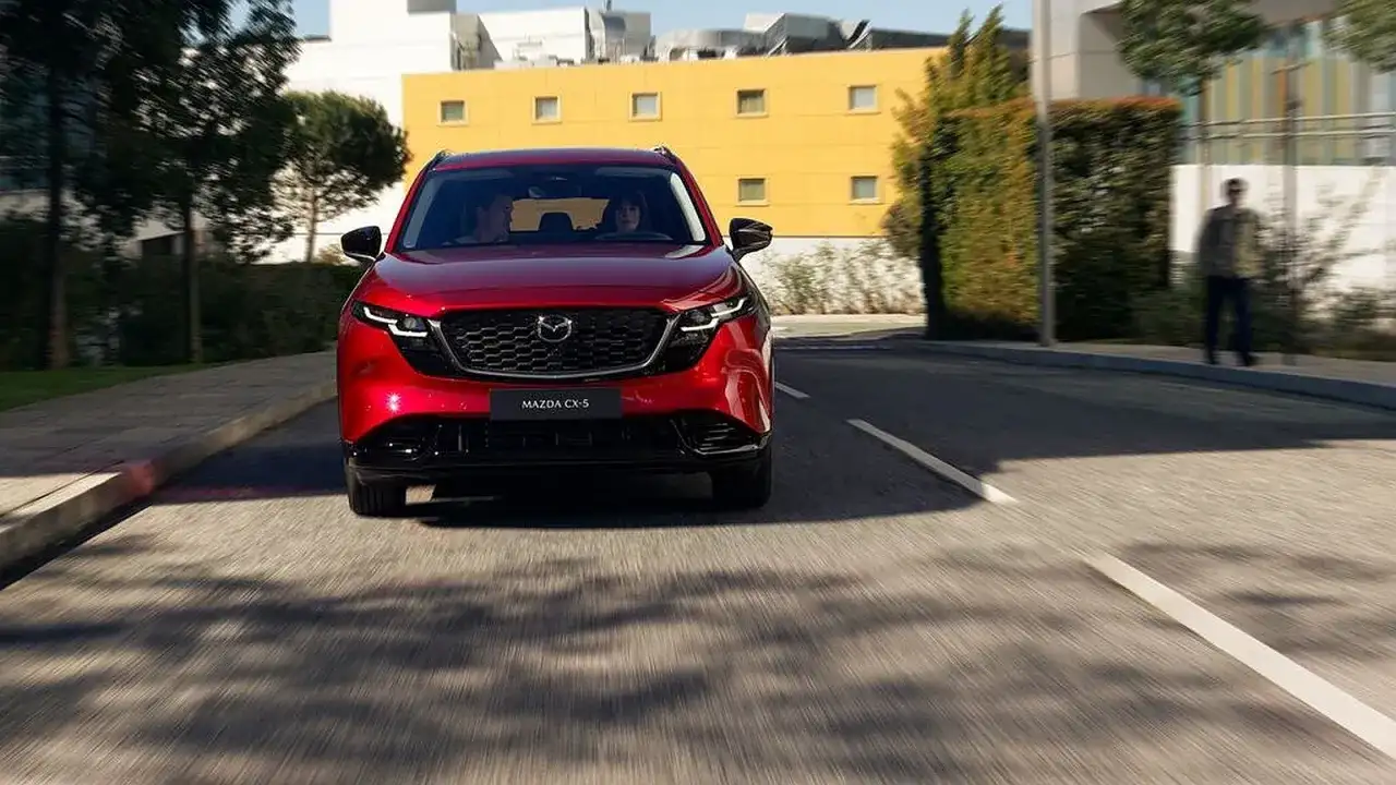 Czerwona Mazda CX-5 jedzie ulicą. W tle budynki i drzewa.