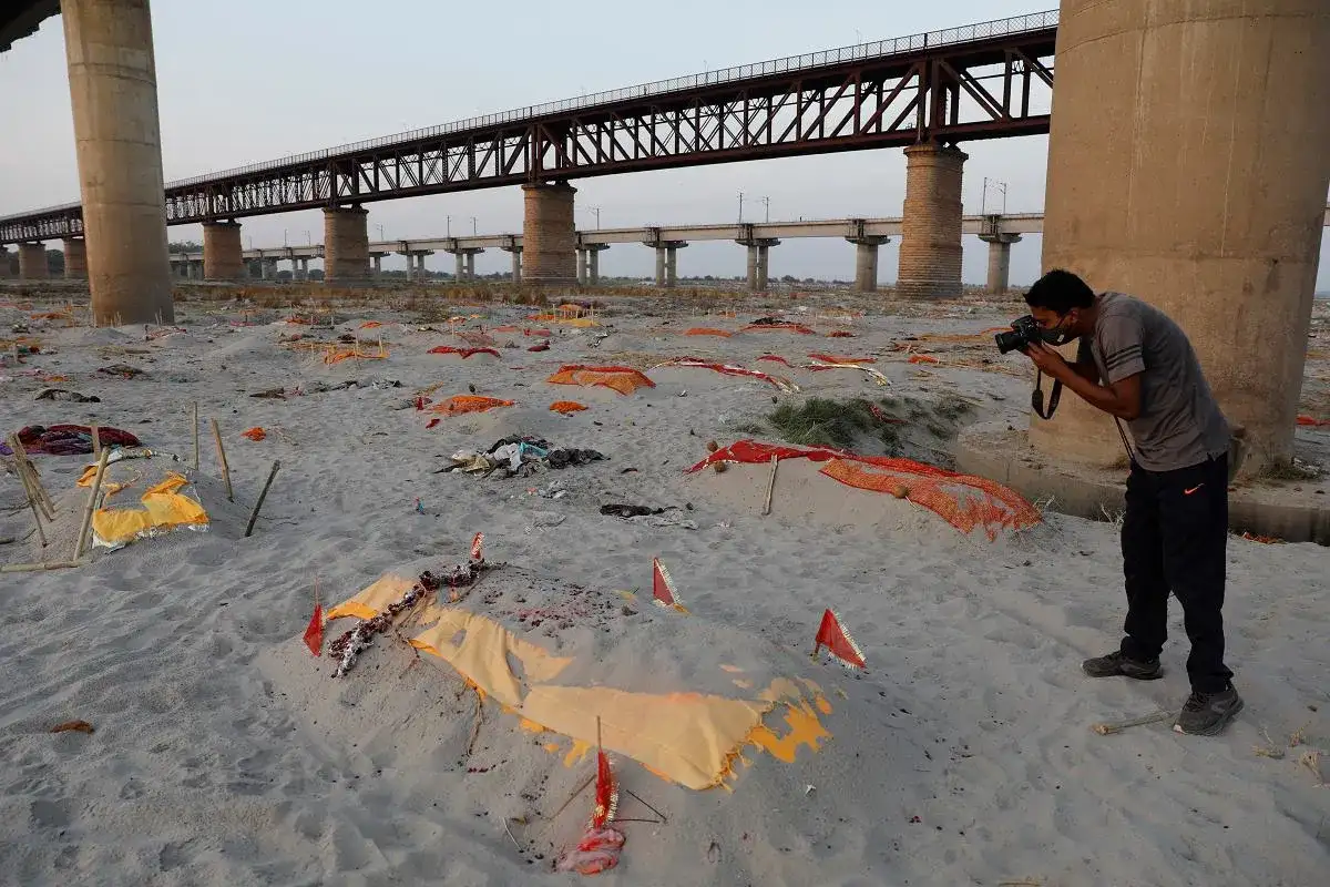 Brzeg rzeki Ganges, gdzie leżą przykryte materiałem ciała, tworzy widok przypominający cmentarzysko. Fotograf dokumentuje tę smutną rzeczywistość.
