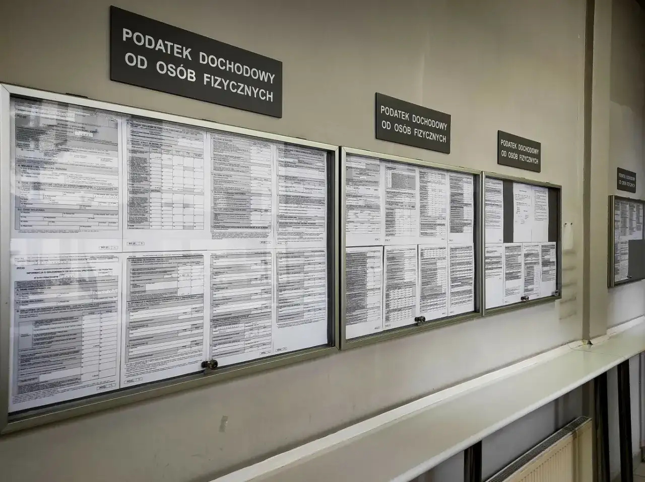 Tablice informacyjne z drukami PIT i informacjami o podatku dochodowym od osób fizycznych. Widać napisy "Podatek dochodowy od osób fizycznych", a także formularze, które mogą dotyczyć 3 progu podatkowego.