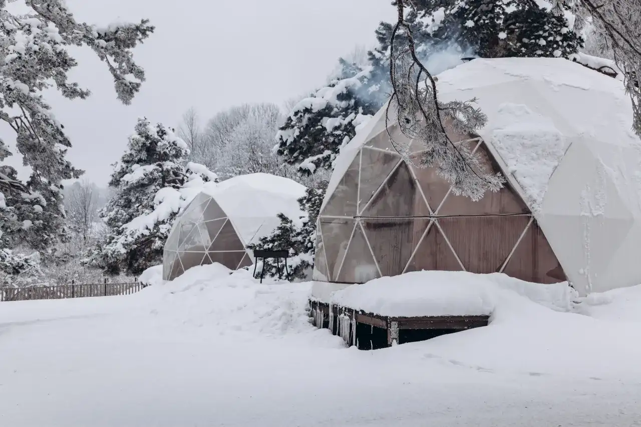 Śnieżne krajobrazy i przytulne domki do wynajęcia na weekend. Dym unosi się z komina jednego z igloo, zapraszając do środka.