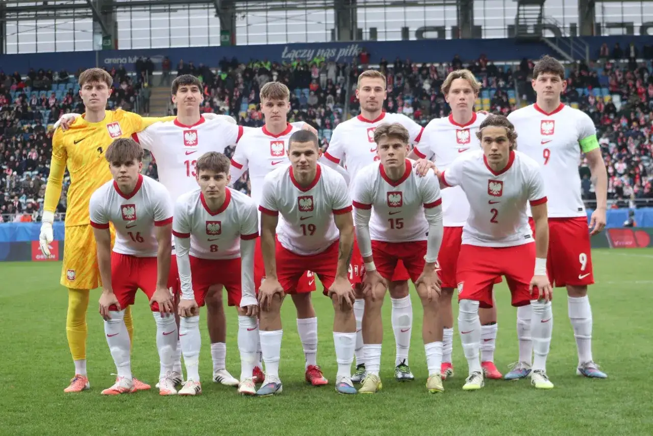 Młoda drużyna piłkarska w biało-czerwonych strojach, gotowa do gry. W tle trybuny stadionu, gdzie kibice dopingują lublin klub piłkarski.