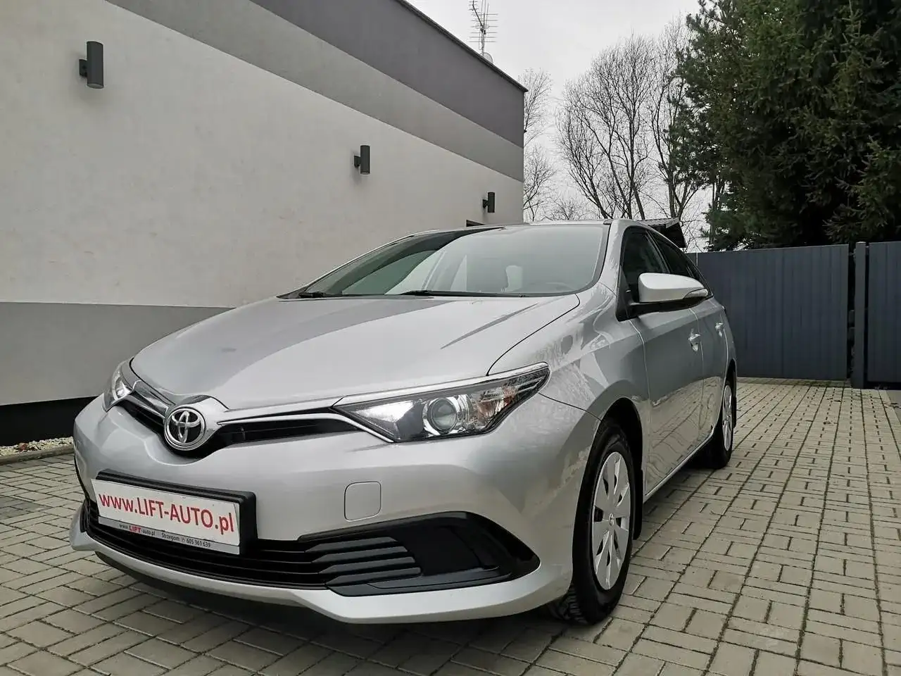Srebrna Toyota Auris 1.6 benzyna zaparkowana na podjeździe z kostki brukowej.