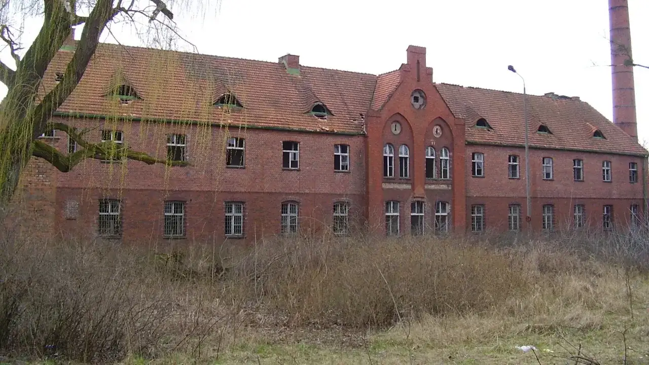 Opuszczony ceglany budynek z charakterystycznymi lukarnami i kominem. Wygląda jak jedno z tych strasznych miejsc, które kryją mroczne historie.