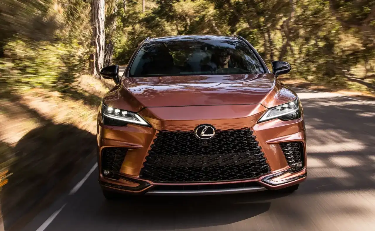 Miedziany Lexus RX 450h pędzi leśną drogą, światła LED rozświetlają trasę.