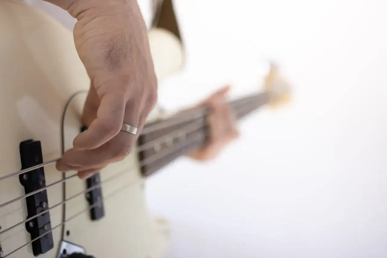 Dłoń z pierścionkiem ćwiczy naukę gry na gitarze basowej, szarpiąc struny.