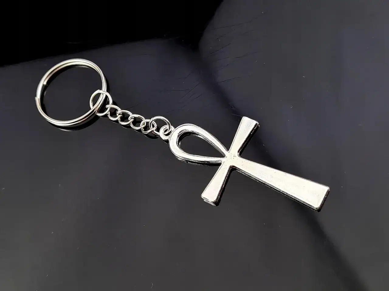 Srebrny brelok z symbolem ankh, starożytnym egipskim znakiem życia, na czarnym tle.