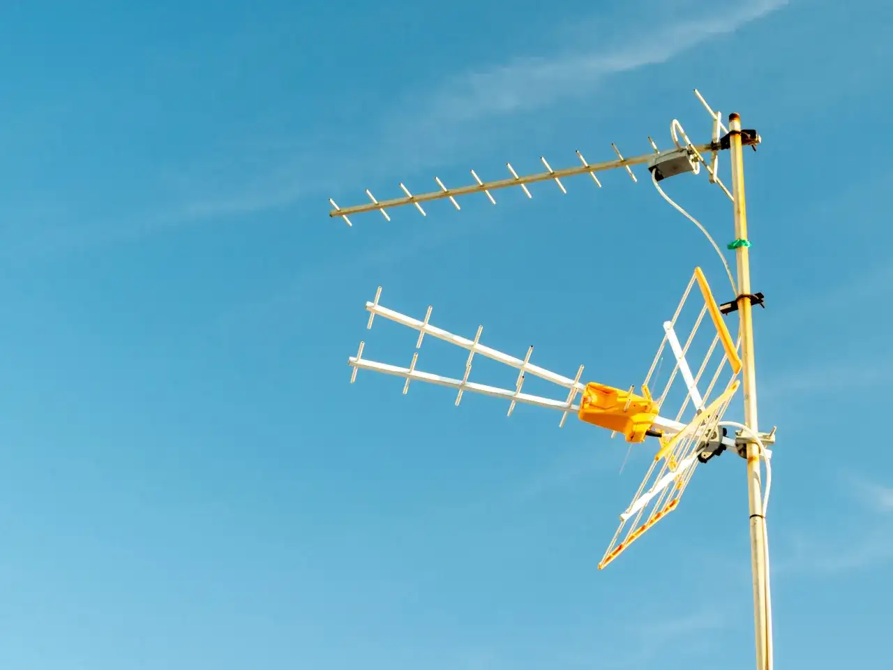 Antena TV z żółtym elementem na tle błękitnego nieba.