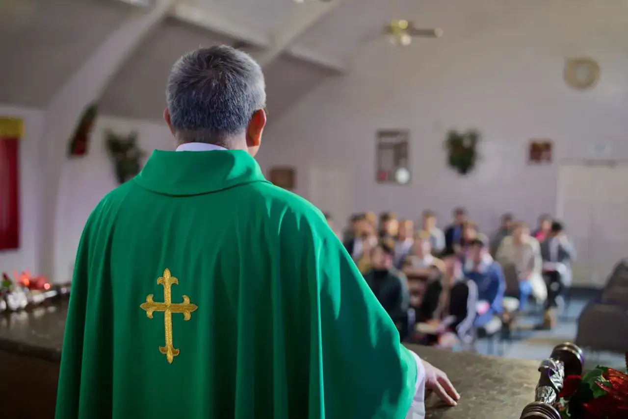 Ksiądz w zielonej szacie z krzyżem, przed wiernymi. Rozważania o skutkach ekskomuniki, czym jest i kogo może dotyczyć.