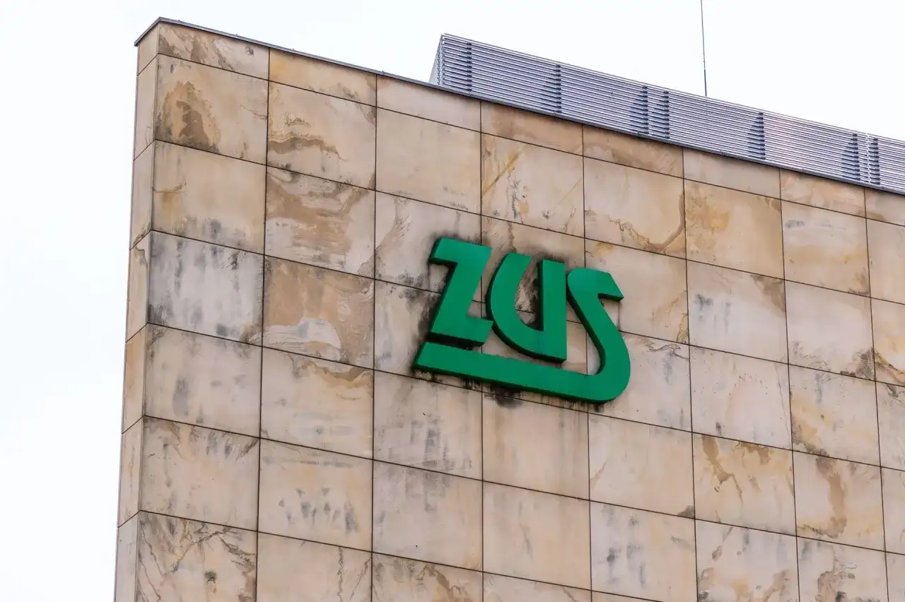 Zielone logo ZUS na beżowej, kamiennej elewacji budynku.