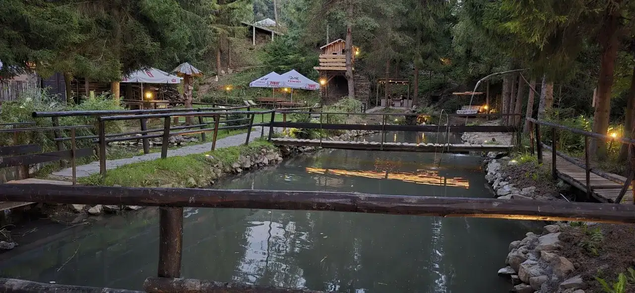 Malownicza okolica bobcikowa chata Szczawnica z drewnianymi mostkami nad strumieniem i oświetlonymi altanami.