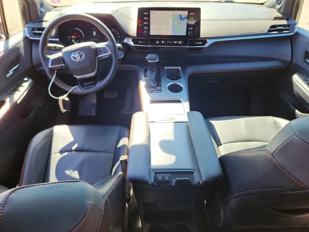 Wnętrze Toyoty Sienna Hybrid: czarne skórzane fotele, kierownica, deska rozdzielcza z ekranem nawigacji.