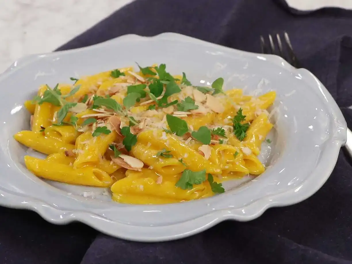 En krämig pasta milanese med mandelspån och färska örter, serverad i en ljusblå skål.
