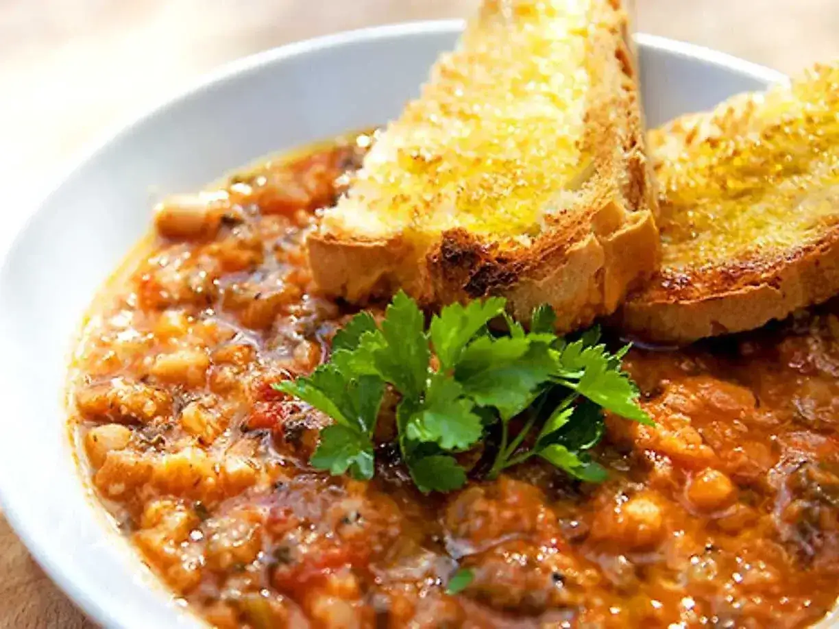 En mustig gryta med bönor och tomater, toppad med rostat bröd och persilja. Perfekt för ett enkelt svartkål recept.