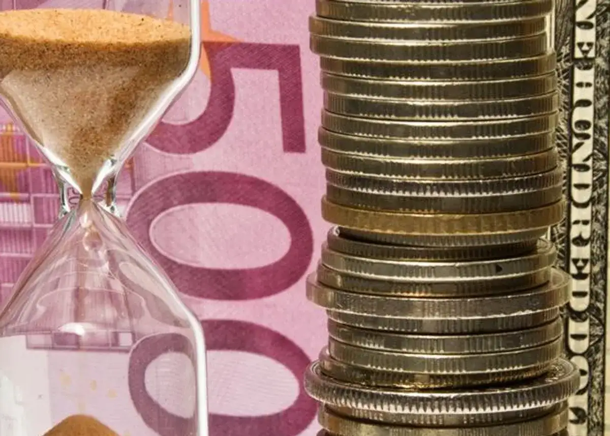 Klepsydra i stos monet na tle banknotu 500 euro. Czy numizmaty co to, to tylko monety?