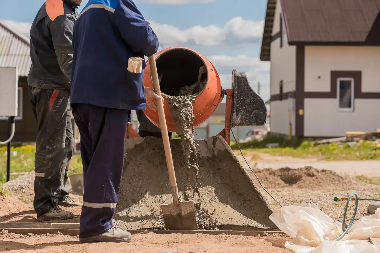 Robotnicy mieszają beton. Widać, ile piasku na kubik betonu jest potrzebne do uzyskania odpowiedniej konsystencji.