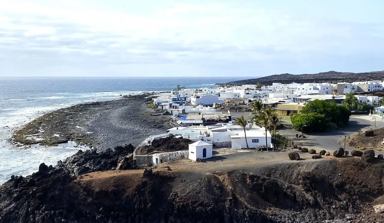 Pueblo blanco costero con mar azul y rocas volcánicas. Un ejemplo de las cosas que ver en Lanzarote.