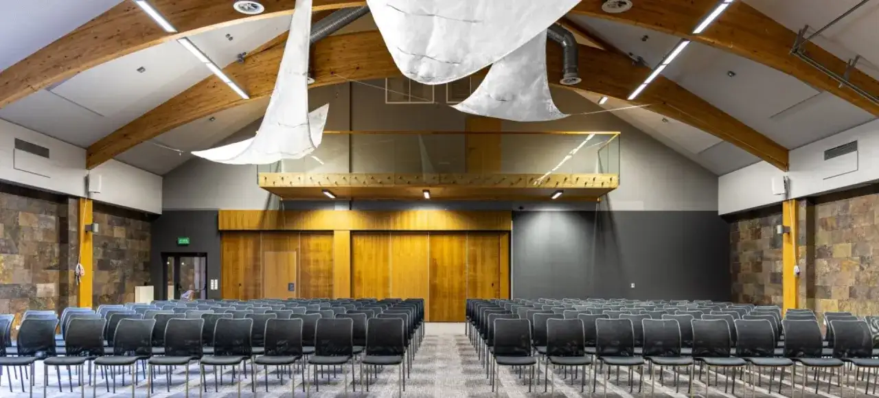 Nowoczesna sala konferencyjna z rzędami czarnych krzeseł, drewnianymi elementami i kamienną ścianą. Idealne miejsce na konferencje na Mazurach.