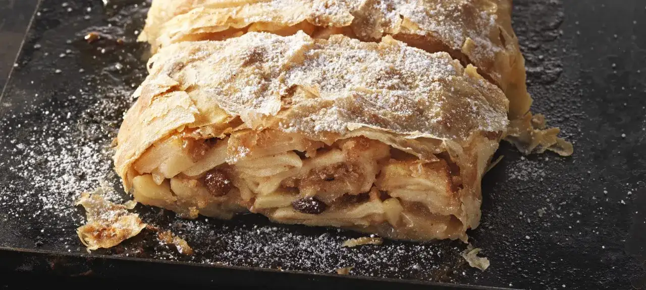 Ein saftiger Apfelstrudel, bestäubt mit Puderzucker, wartet darauf, nach diesem Apfelstrudel Rezept zubereitet zu werden.