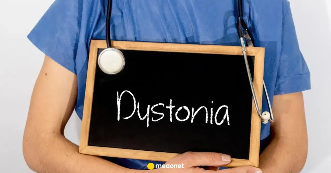 Lekarz w niebieskiej koszuli trzyma tabliczkę z napisem "Dystonia". Stetoskop zwisa na jego ramieniu.