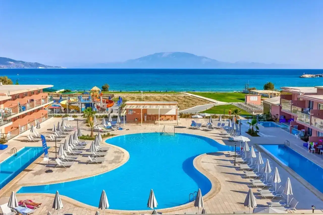 Słoneczny dzień w Alykanas Beach Hotel. Baseny, zjeżdżalnie wodne i leżaki czekają na gości. W tle błękitne morze i góry.