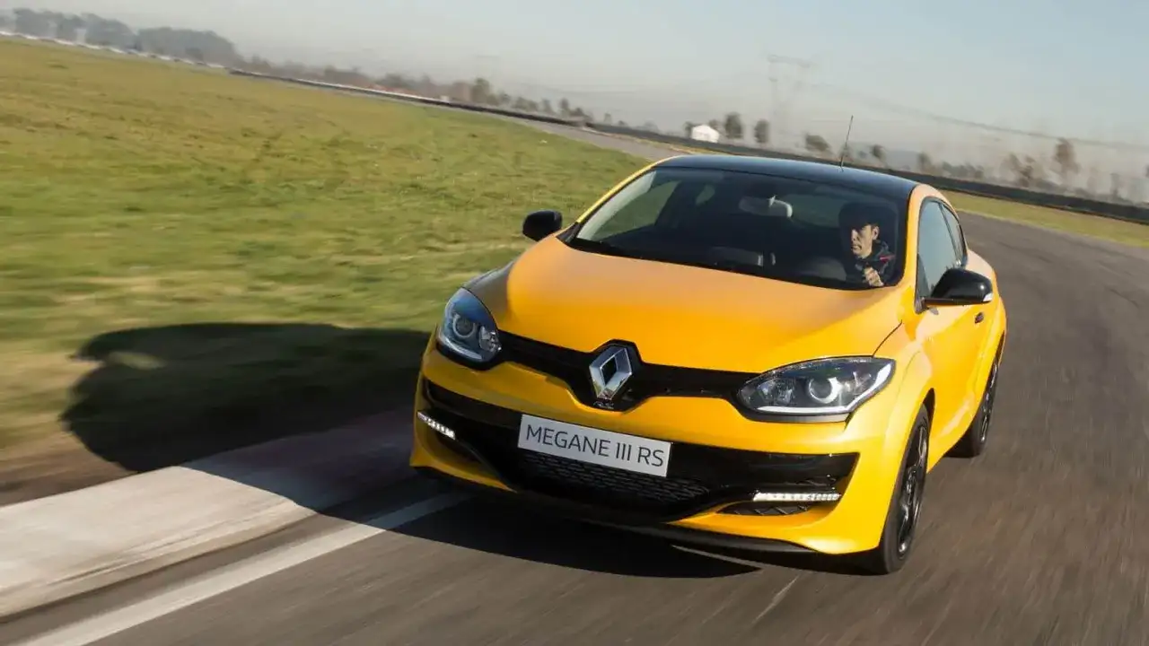 Żółty Megane RS na torze wyścigowym, kierowca w czapce z daszkiem za kierownicą.