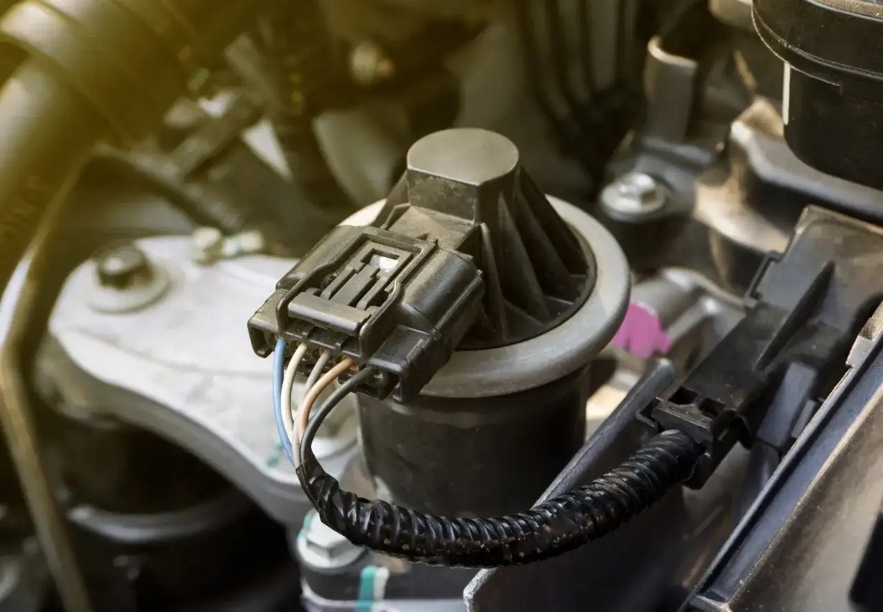 Composant noir avec connecteur électrique et fils colorés, partie d'une vanne EGR dans un compartiment moteur.