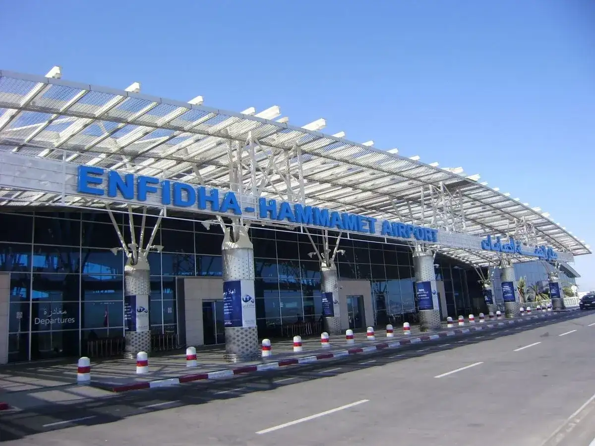 Nowoczesny budynek lotniska Enfidha-Hammamet w Tunezji, z niebieskimi literami nazwy i przeszkloną fasadą.